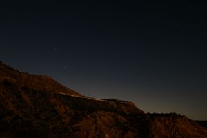 Rugged mountain silhouette against a dark starlit sky with a faint glow on the horizon.