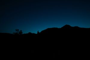 A silhouette of mountains against a dark blue night sky with stars visible in the background.