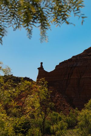 Red sandstone cliffs and rock formations rise against a bright blue sky with green foliage in the foreground.