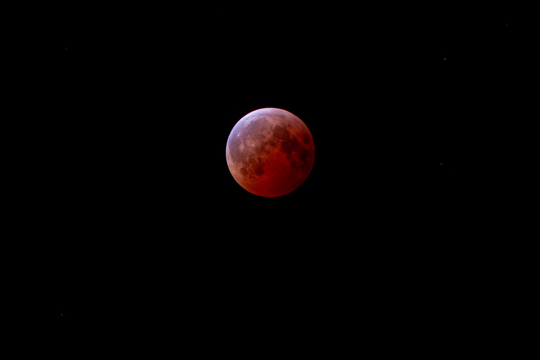 A blood red full moon during a total lunar eclipse glows brightly against the black night sky.