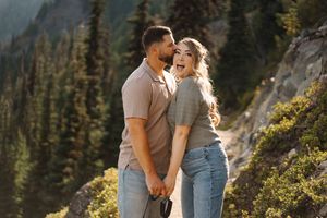 A couple shares a romantic moment while hiking in a scenic mountain landscape with evergreen trees.
