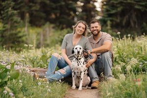A series of outdoor photos showing a couple sitting on a log with their spotted dog in a wildflower meadow at sunset.