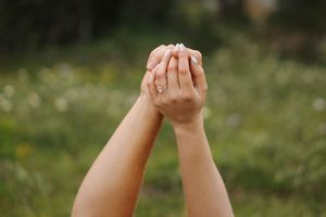 Raised hands interlock fingers against a bright natural outdoor background.