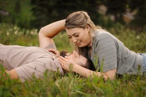 A couple lying in a grassy meadow share tender moments together in a romantic outdoor photoshoot.