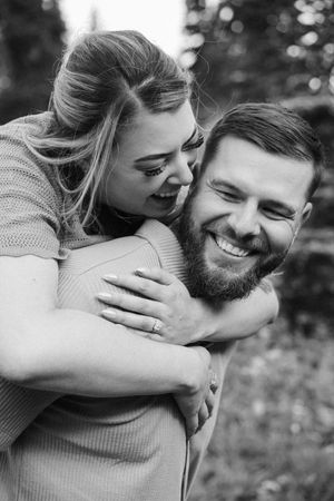 Joyful candid black and white photo of couple sharing a playful piggyback moment outdoors.