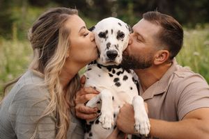 A couple poses with their spotted Dalmatian puppy in a park setting during a photo session.