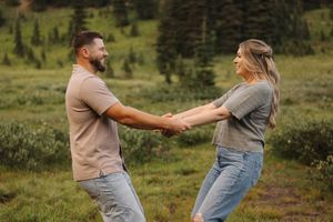Two people playfully dance together in a grassy meadow with mountains in the background.