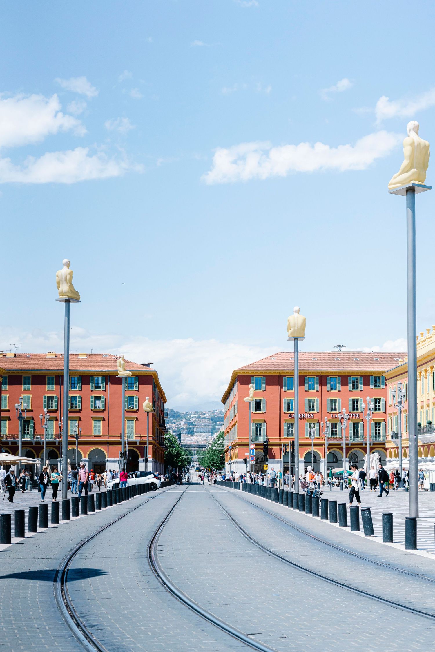 Tram tracks lead through Place Massena square in Nice, France with iconic red buildings and decorative lamp posts.