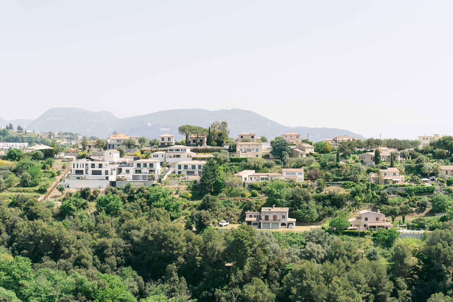 Panoramic view of a Mediterranean hillside town with white buildings nestled among lush greenery and mountains.