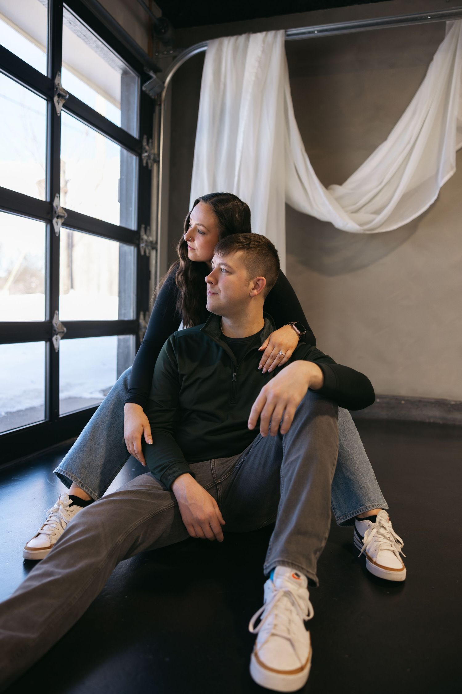 A couple sitting by a window in casual wear, sharing an intimate moment.