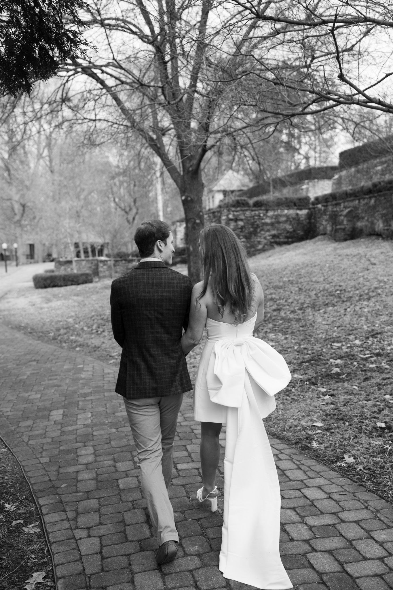 A couple walking along a brick path on a misty day with bare trees and stone walls in the background.