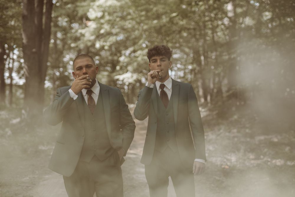 Two people in dark suits standing in misty forest setting.
