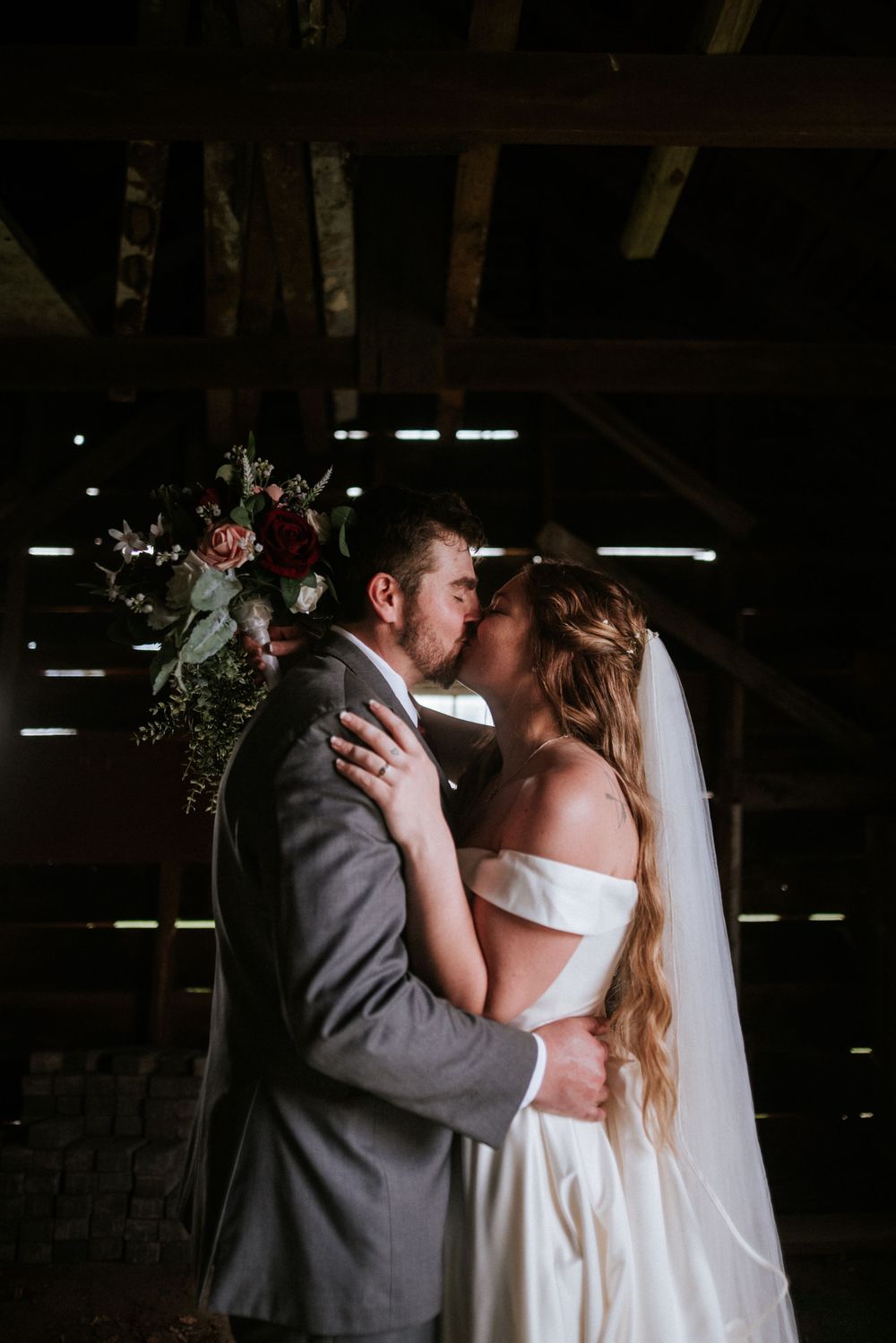 A couple shares their first kiss in a rustic barn setting with dramatic lighting.