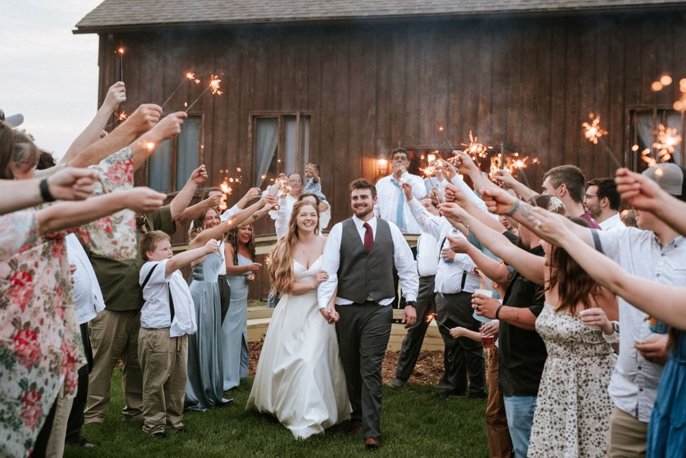 Wedding exit with guests raising sparklers as couple walks through at rustic venue.