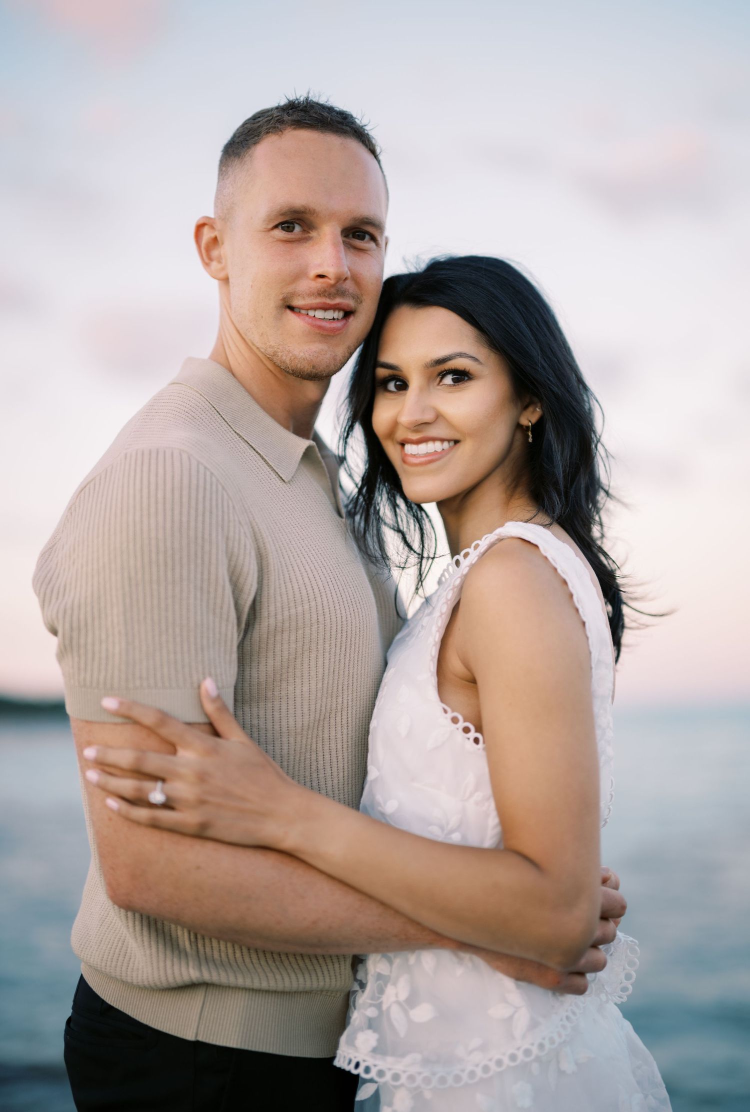 Couple poses together by the water during golden hour in casual elegant attire.