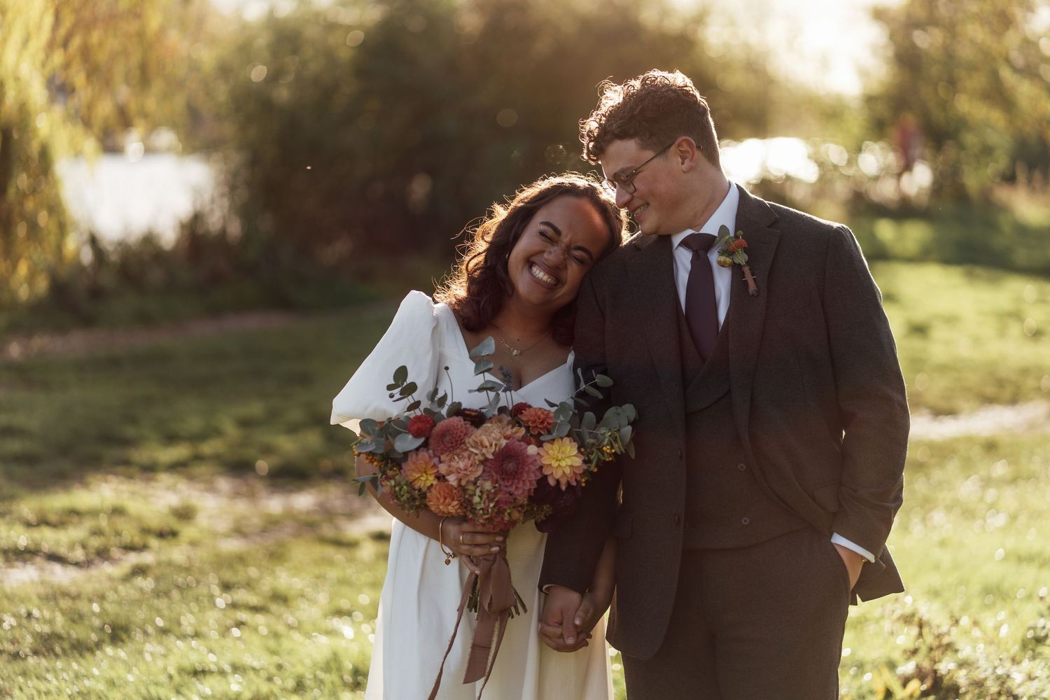 Playful wedding couple posing by vintage red double-decker bus in urban setting.