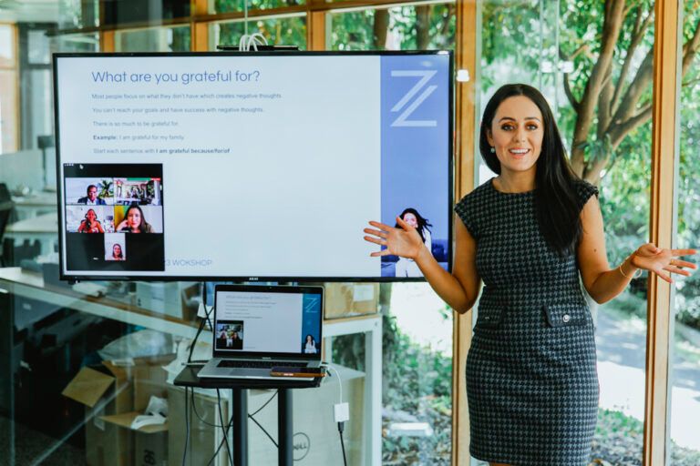 Professional presenter giving a business presentation in front of a digital display screen in a bright modern office setting.