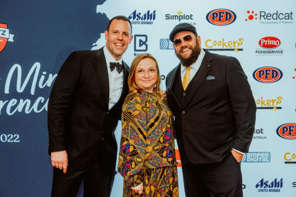 Three people posing at a music industry awards event with sponsor logos in the background.