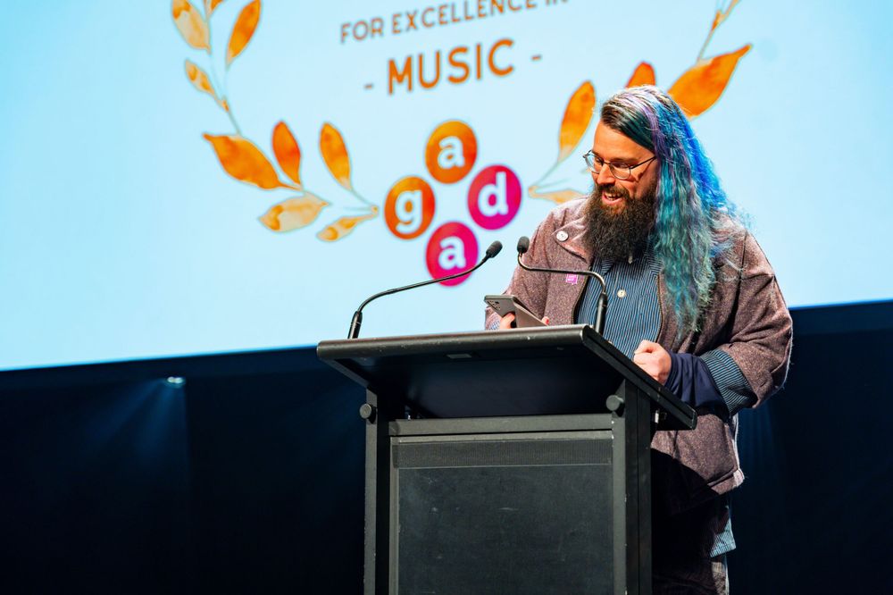 Speaker at a music industry podium with a banner showing excellence in music.