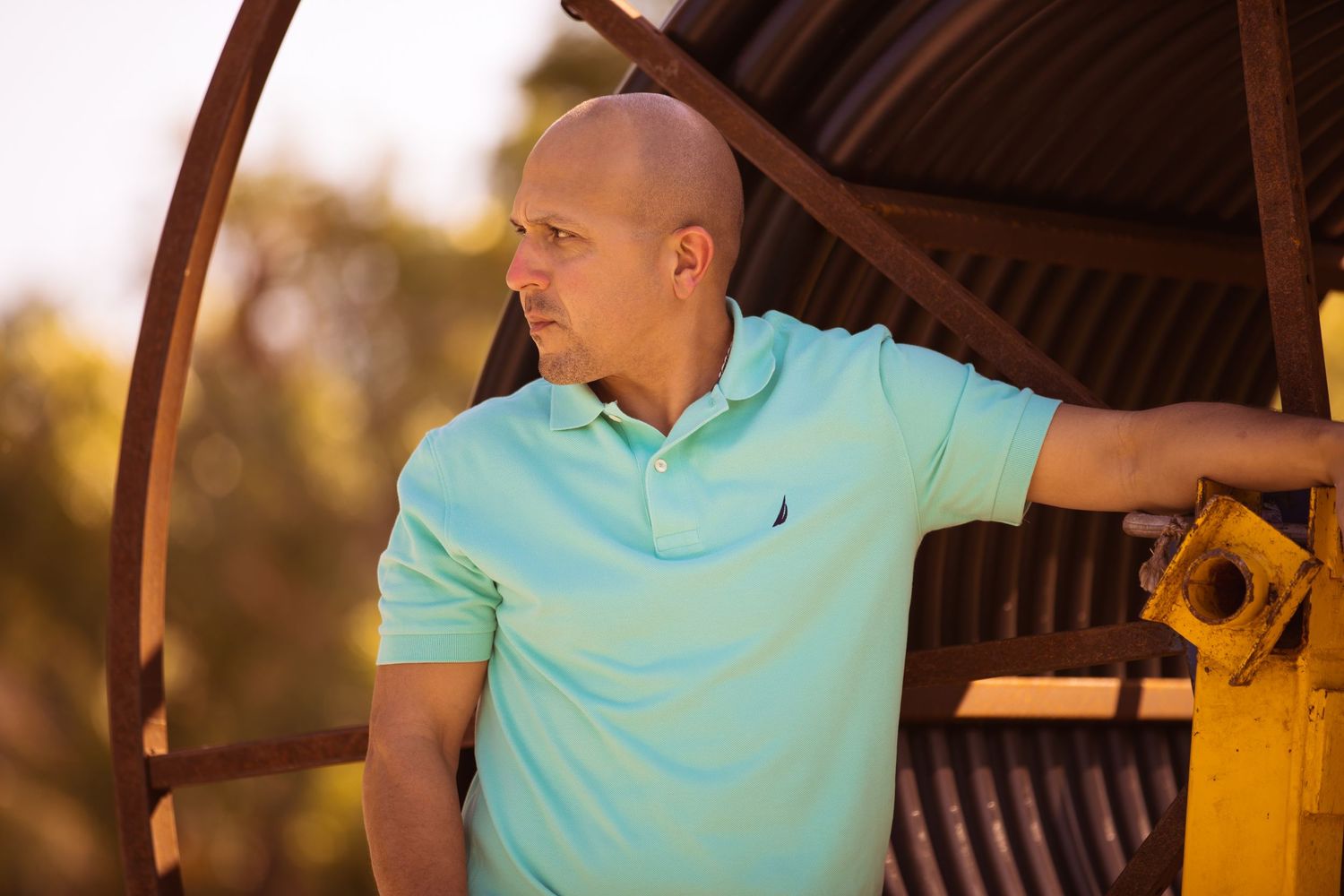 Person in light blue polo shirt posing under wooden architectural structure at sunset.