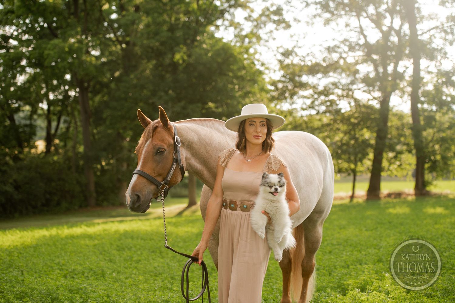 Light-colored dress and wide-brimmed hat complement the palomino horse in summer meadow setting.