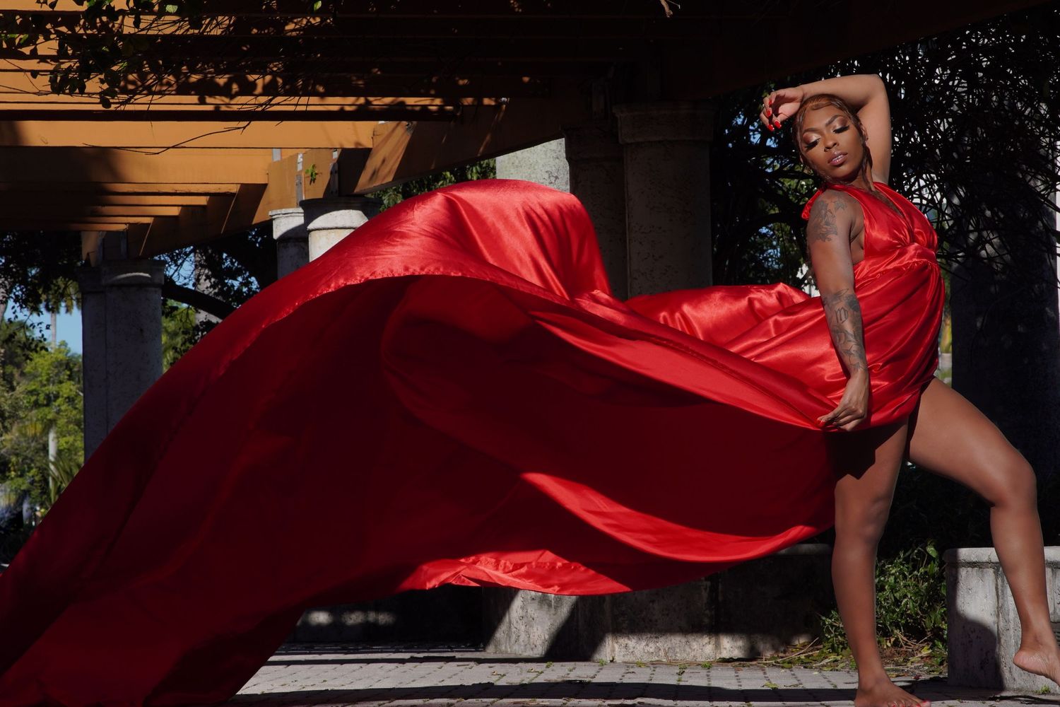Vibrant red dress billows dramatically during outdoor photo session under architecture.