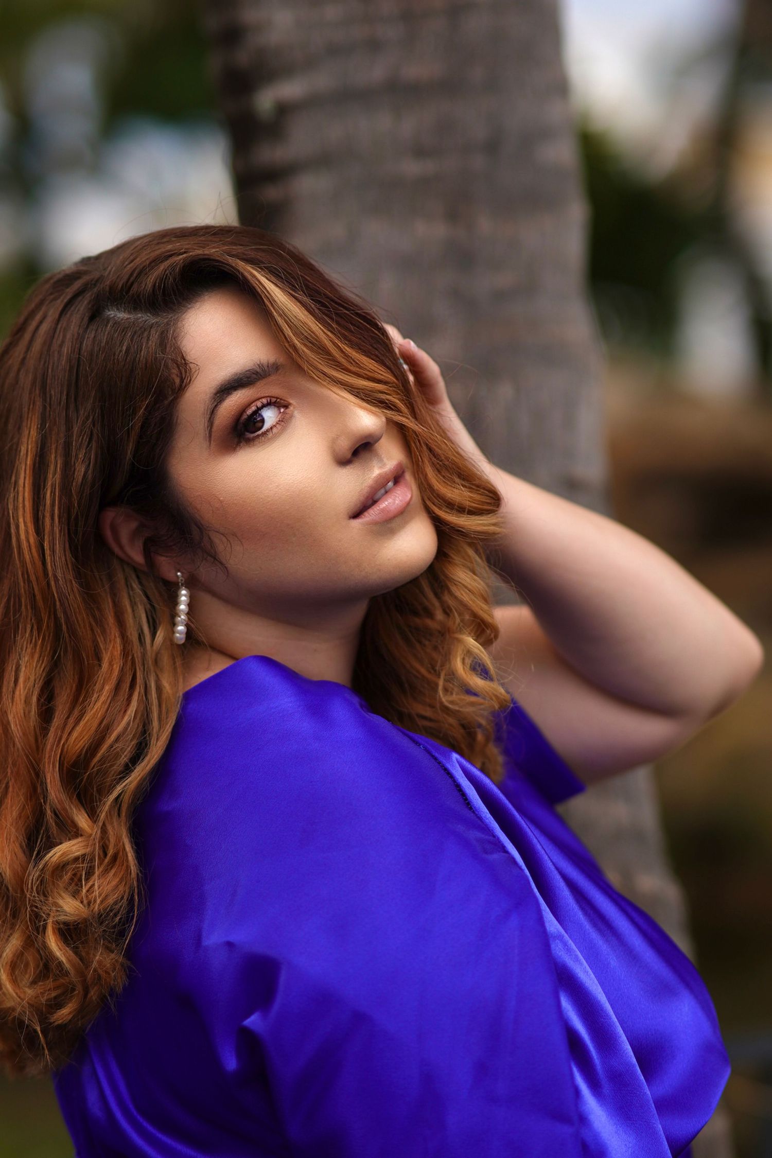 Portrait in royal blue blouse with flowing hair against palm tree background.