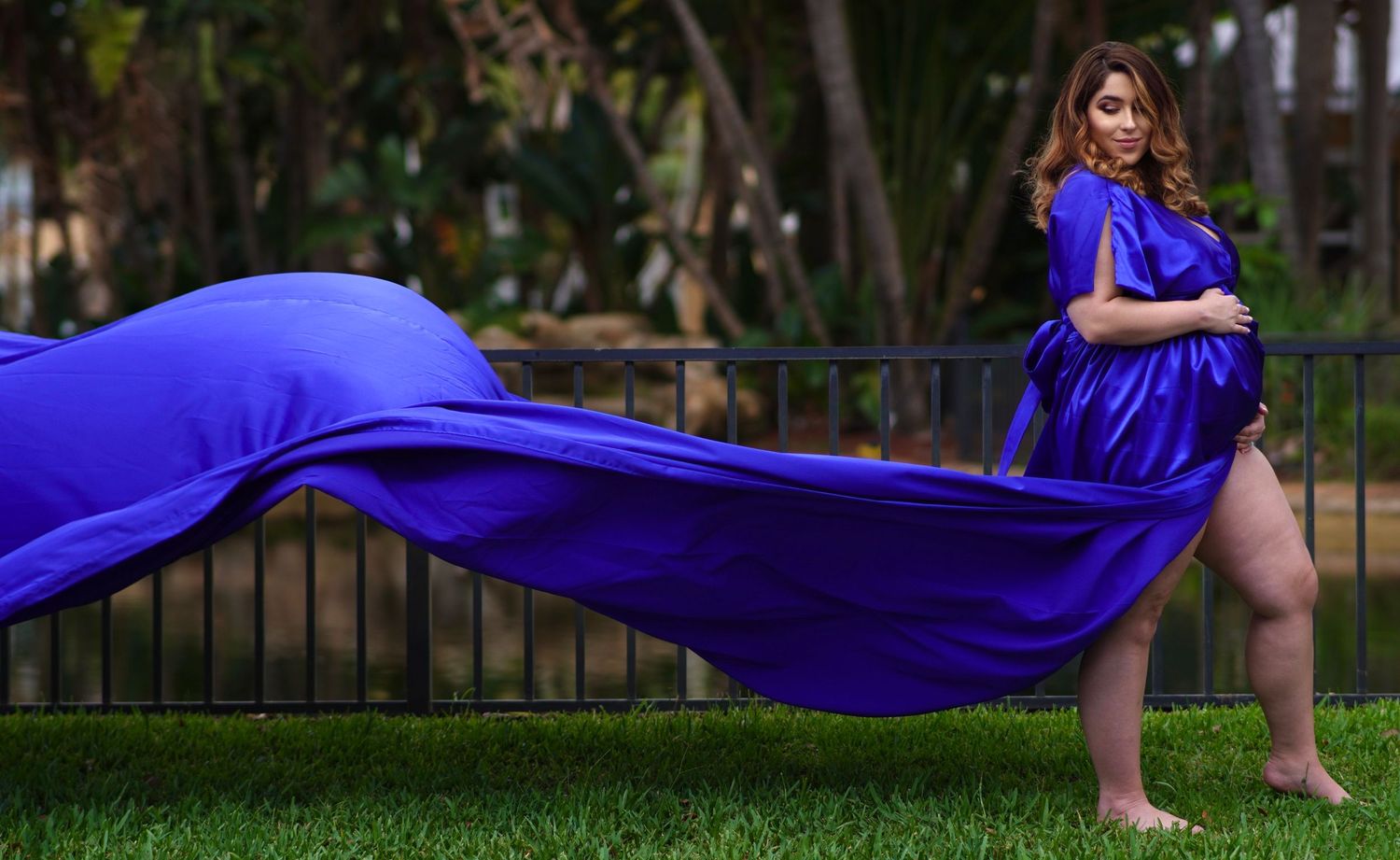 Long flowing purple dress catches wind in outdoor garden photoshoot.