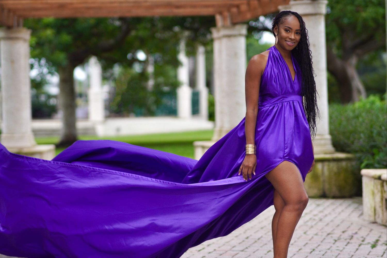 Flowing purple silk gown creates dramatic movement against stone colonnade.