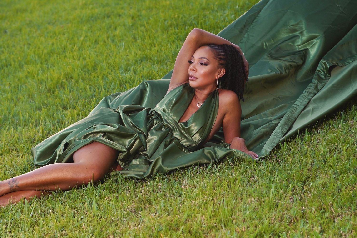 Flowing green silk dress drapes elegantly across grass in outdoor fashion photo.