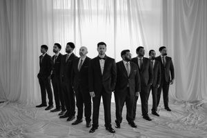 A group of formally dressed people standing in a line against a white curtain backdrop.