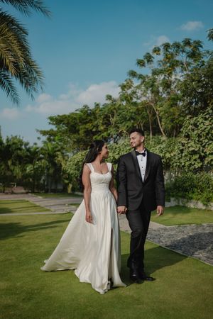 A couple in wedding attire walks together on a scenic palm-lined path at a tropical outdoor venue on a sunny day.