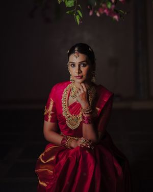 Traditional South Indian bride wearing a deep red silk saree and ornate gold jewelry in dramatic lighting.