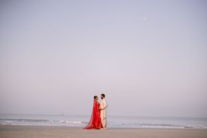 A couple walks along a misty beach shoreline with waves crashing in the background.