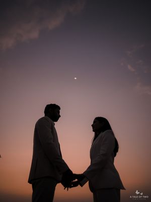 Silhouette of couple holding hands against dusky pink sky with glowing moon.