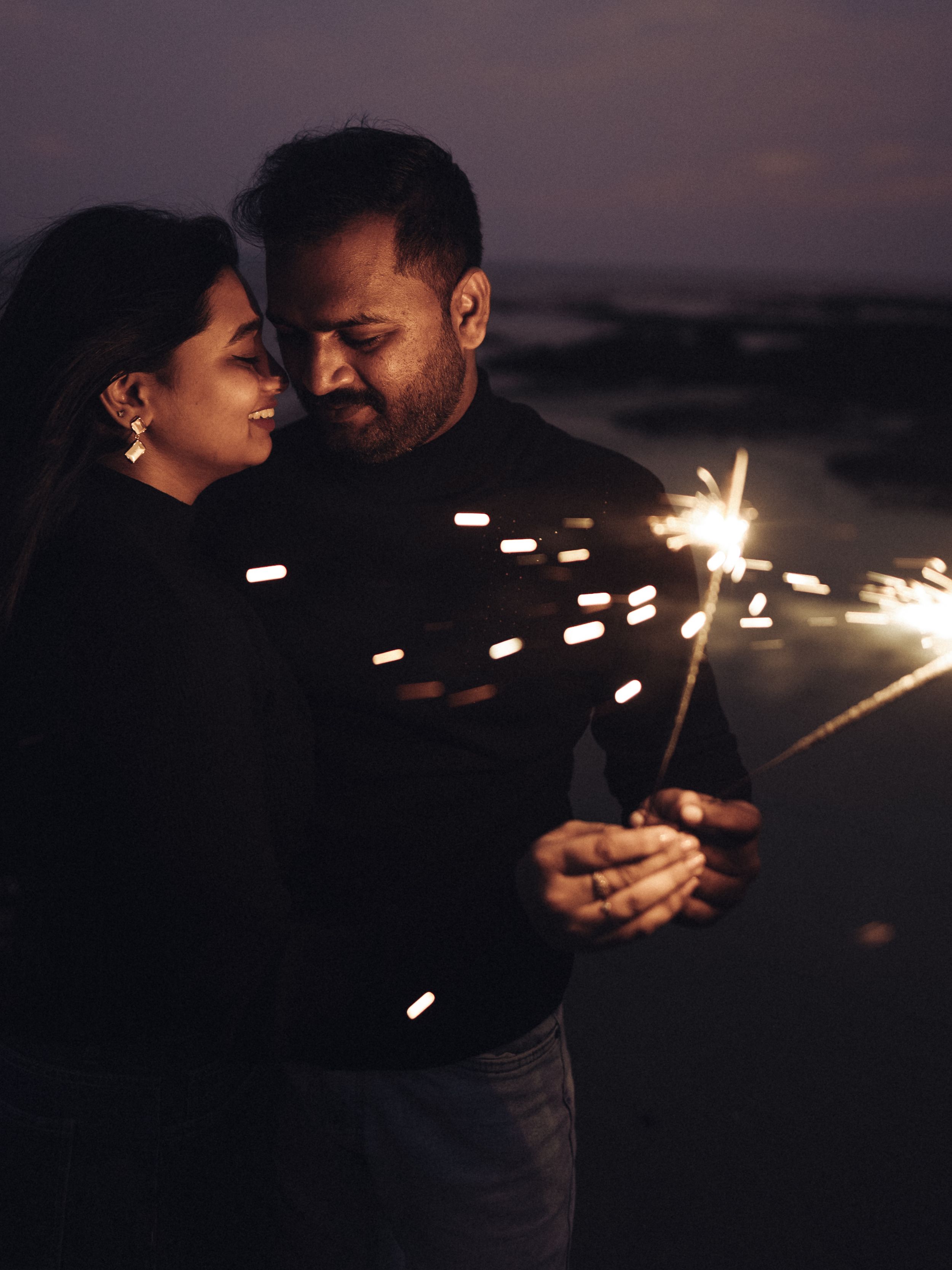 A romantic moment captured with sparklers on a dark beach.