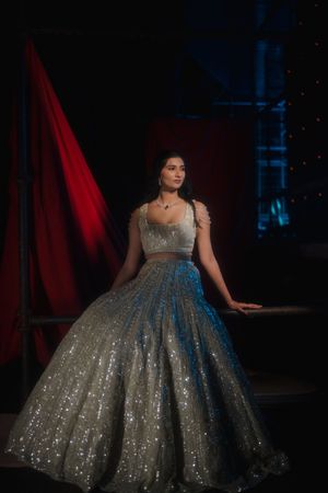 A sparkling silver ball gown with a dramatic silhouette photographed in a dark, moody setting.