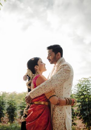 A couple in traditional Indian wedding attire embraces during an outdoor photo session at sunset.