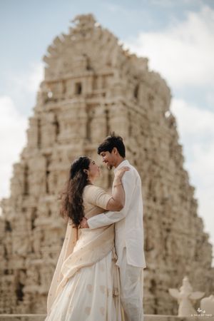 A romantic couple shares an intimate moment in front of a traditional Indian temple's intricately carved facade.