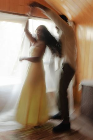 A blurred motion sequence showing a figure in black clothing performing dynamic dance movements against a warm-toned wall.