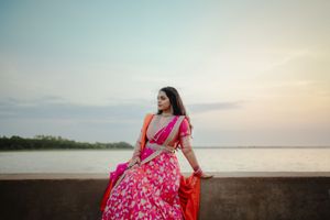 A person in a flowing pink dress poses gracefully against a scenic beach backdrop during golden hour.