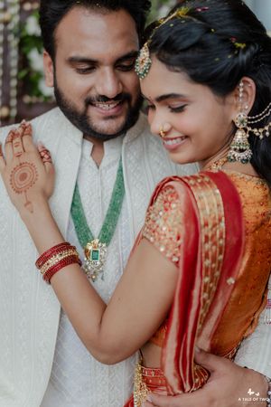 Indian bride and groom in traditional wedding attire, bride wearing red saree and gold jewelry, groom in white sherwani.