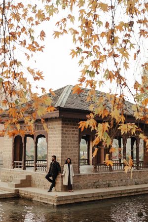 A stone gazebo by a lake with autumn maple leaves framing the scene on a peaceful fall day.