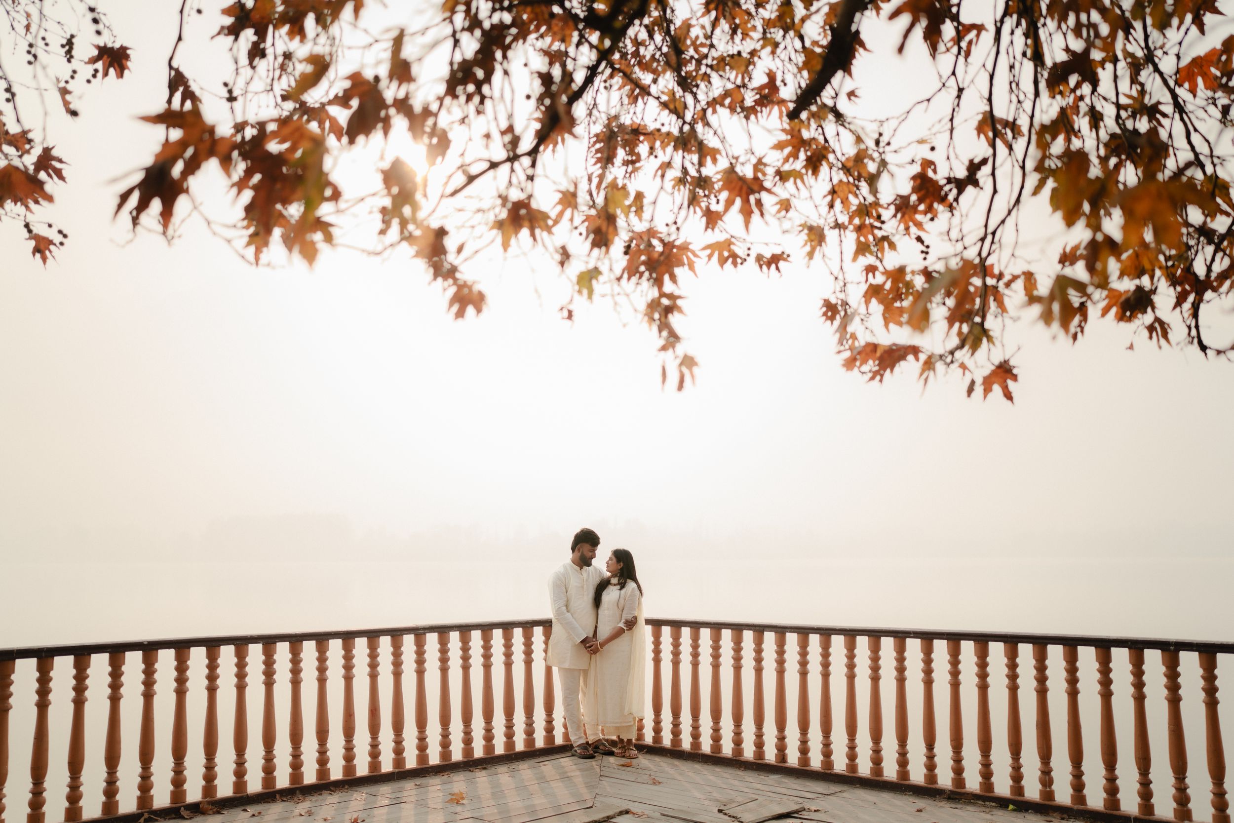A wooden deck overlooks a tranquil lake with autumn trees framing the serene waterfront view.