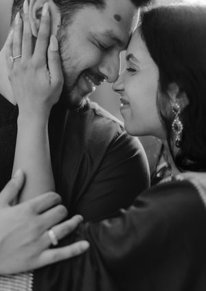 Black and white intimate portrait of a couple sharing a tender romantic moment with hands touching faces and smiles.