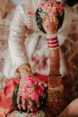 Close-up shots of hands adorned with traditional Indian bridal jewelry and pink rose petals during a wedding ceremony.