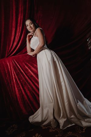 A dramatic bridal portrait series against deep red velvet curtains showcasing an elegant white wedding gown.