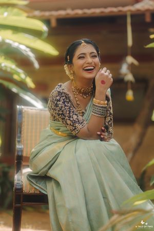 Laughing Indian bride in mint green saree with navy embroidered blouse and gold jewelry at outdoor wedding.
