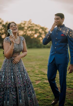 Joyful Indian couple in traditional attire laughing outdoors at golden hour, woman in embroidered lehenga, man in blue sherwani.