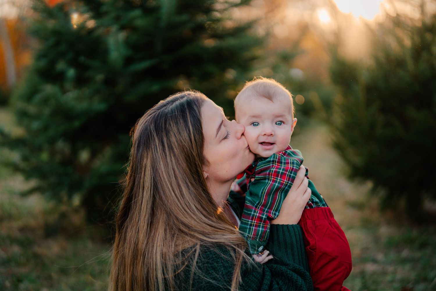 An intimate outdoor portrait with plaid and green clothing against evergreen trees.